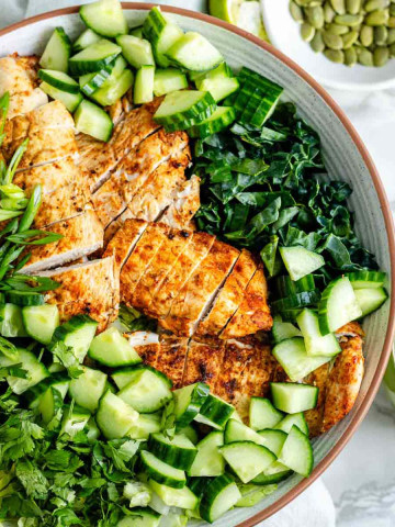 Greens in a bowl with cucumbers and sliced chicken.