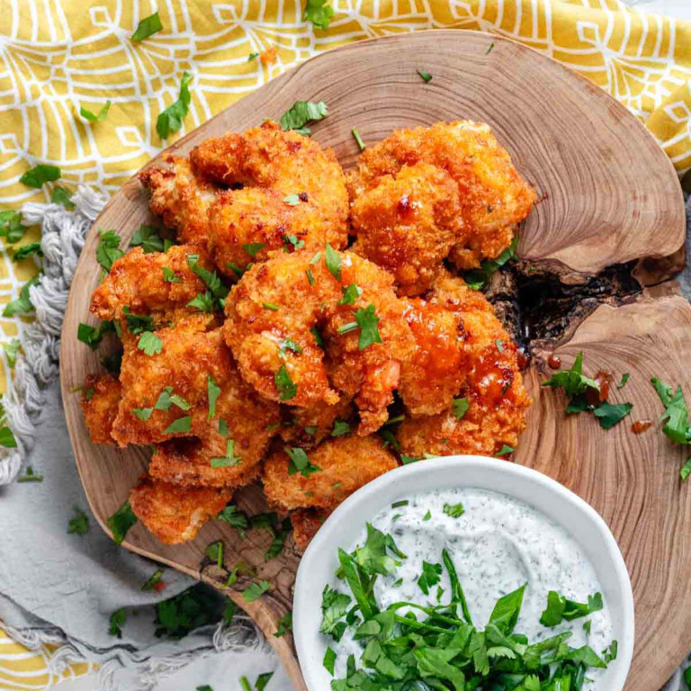 Breaded shrimp coated in orange sauce on a wooden platter garnished with parsley.