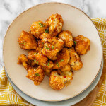 Breaded cauliflower coated in a sauce with sliced green onions on a plate.
