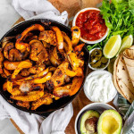 A skillet with grilled strips of chicken and peppers beside bowls of sauce and toppings.