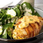 Bacon-wrapped chicken on a plate with a spinach salad.