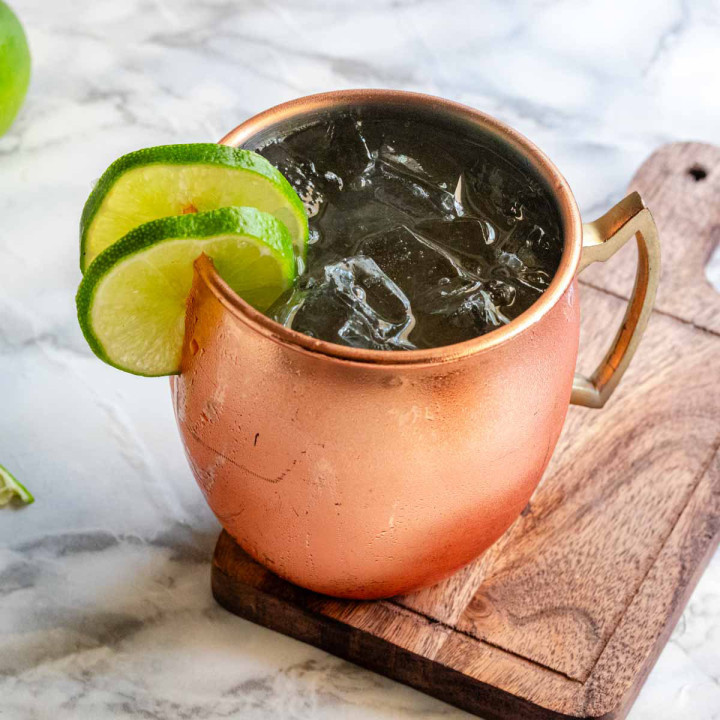 A cocktail with ice in a copper mug garnished with lime wheels.