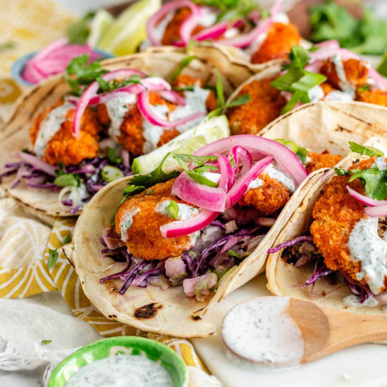 Tacos filled with breaded shrimp, cabbage slaw, pickled red onion, ranch dressing, and cilantro.