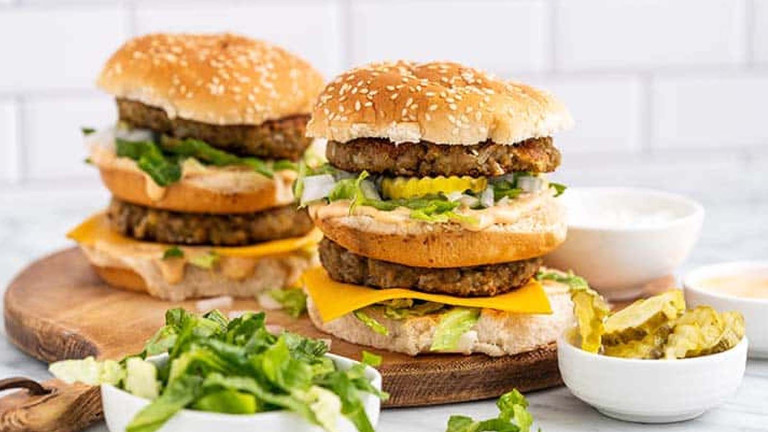 Burgers on a platter with three buns, two patties, cheese, pickles, lettuce, and sauce.