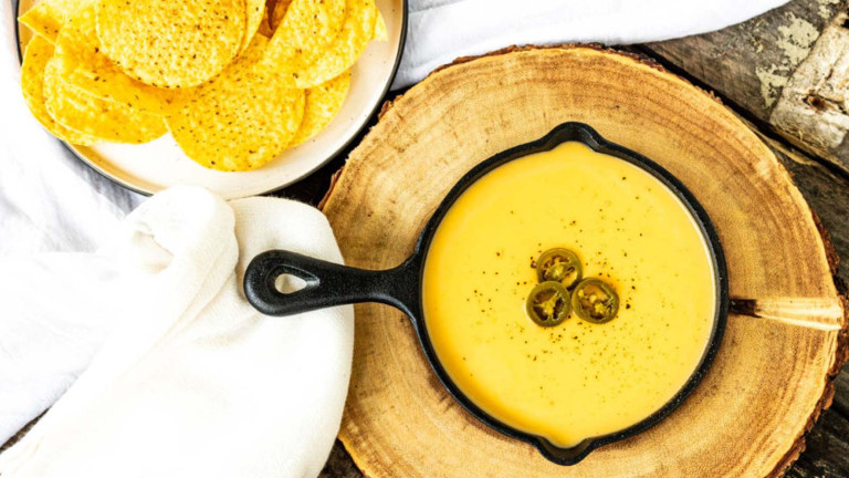 Orange cheese sauce in a small black cast iron skillet beside a bowl of round tortilla chips.