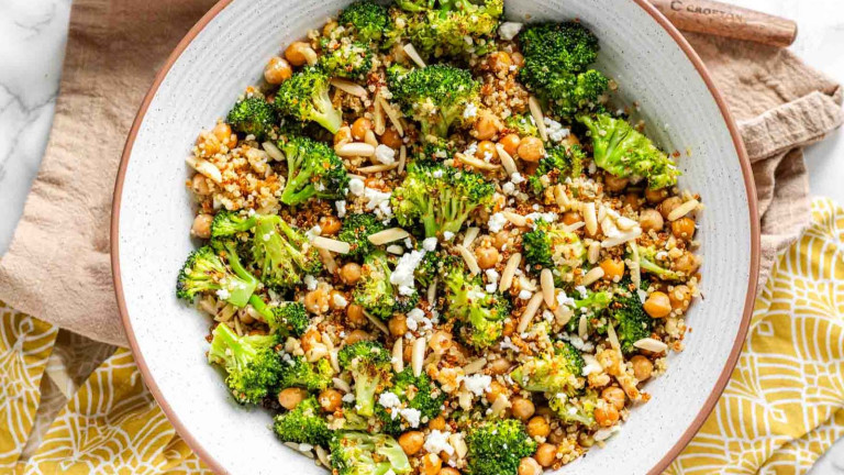 Broccoli salad in a bowl, topped with crumbled goat cheese and slivered almonds.