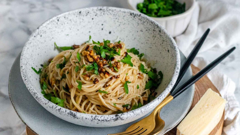 Pasta in a bowl, topped with walnuts and parsley.