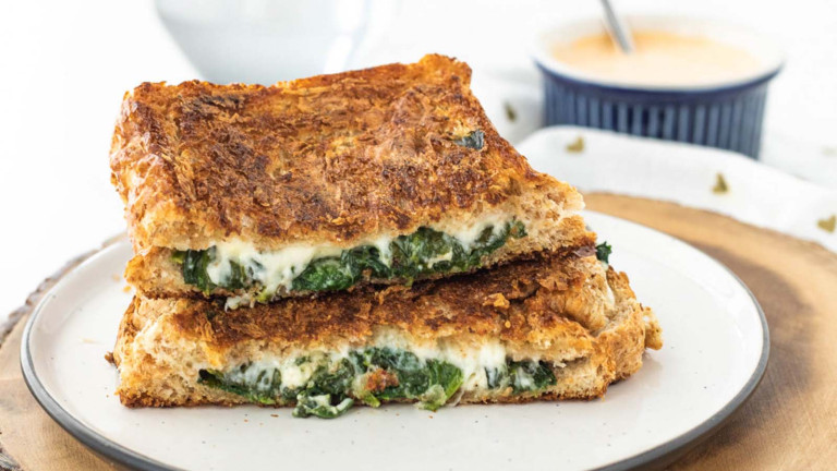 A stacked halved sandwich filled with spinach and cheese.