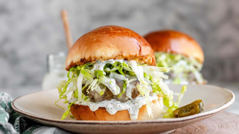 A burger on a bun with lettuce and a drippy sauce.