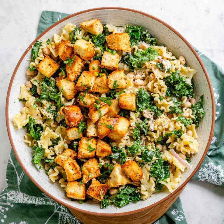 Pasta and greens in a bowl topped with croutons.