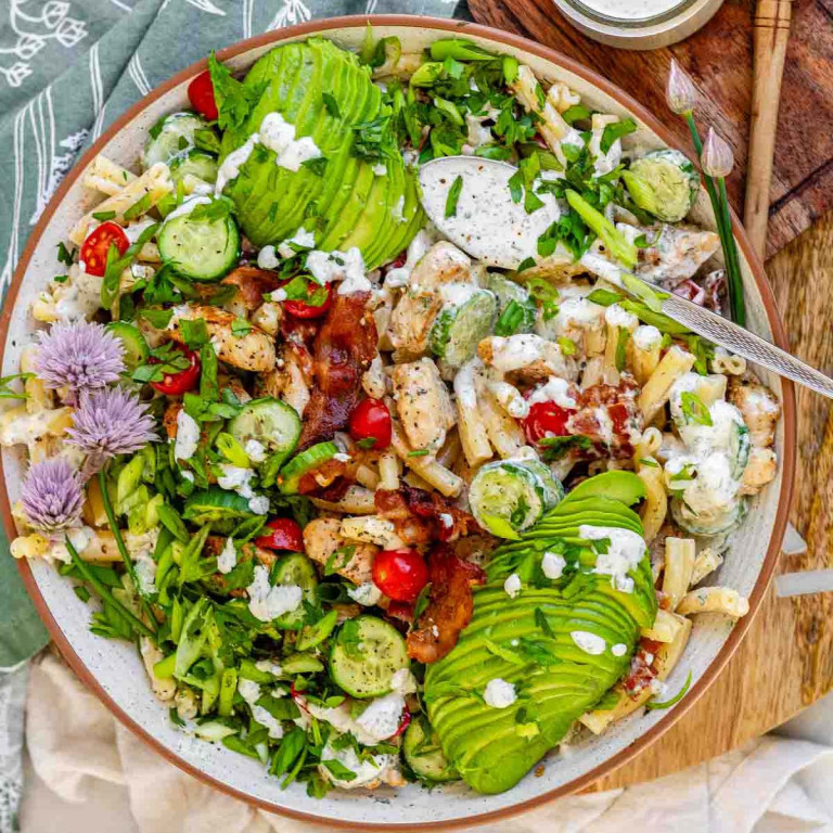 Salad in a bowl topped with sauce, avocado, greens, and green onion flowers.