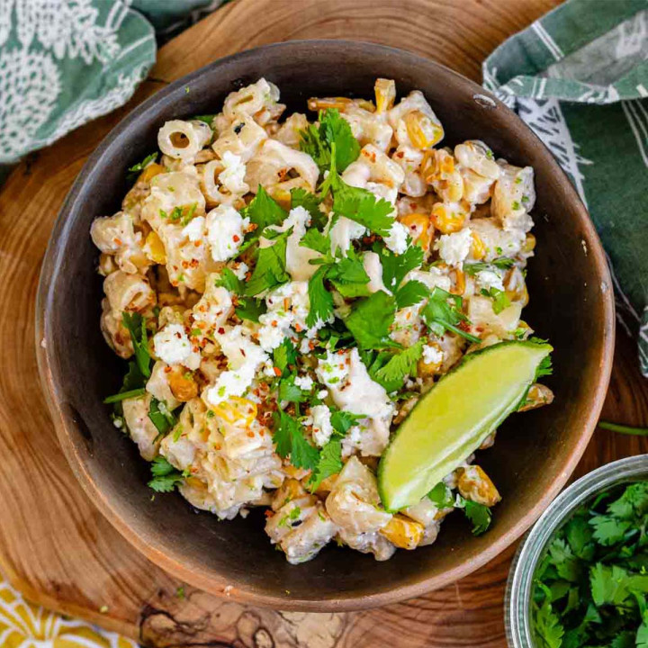 Pasta salad in a bowl topped with cheese, chili flakes, and cilantro with a lime wedge.