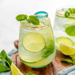 A glass with a bubbly drink garnished with lime slices and mint leaves.