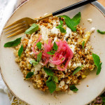 Bulgur and lentil pilaf on a plate with a fork topped with tahini, oregano leaves, and pickled red onions.