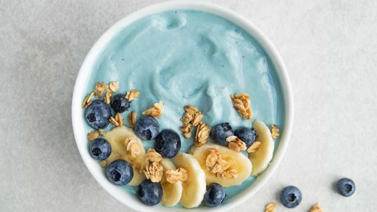 A blue smoothie bowl topped with banana slices, blueberries, and oats.