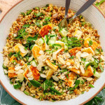 A couscous lentil salad in a bowl topped with grilled halloumi, almond slices, cucumber, and herbs.