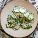 Sliced cucumber on a plate with sauce, topped with seeds and chives.