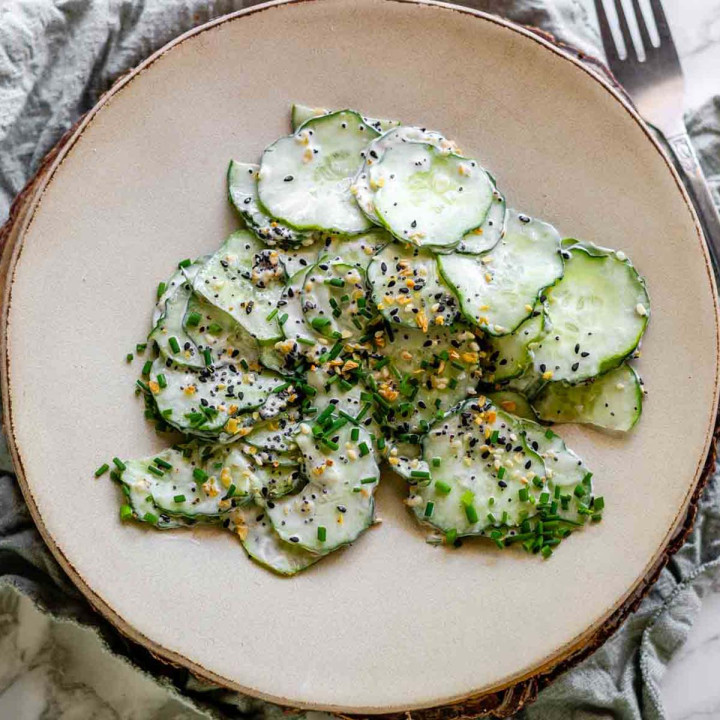 Sliced cucumber on a plate with sauce, topped with seeds and chives.