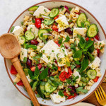 Salad in a bowl topped with squares of feta cheese and fresh herbs.