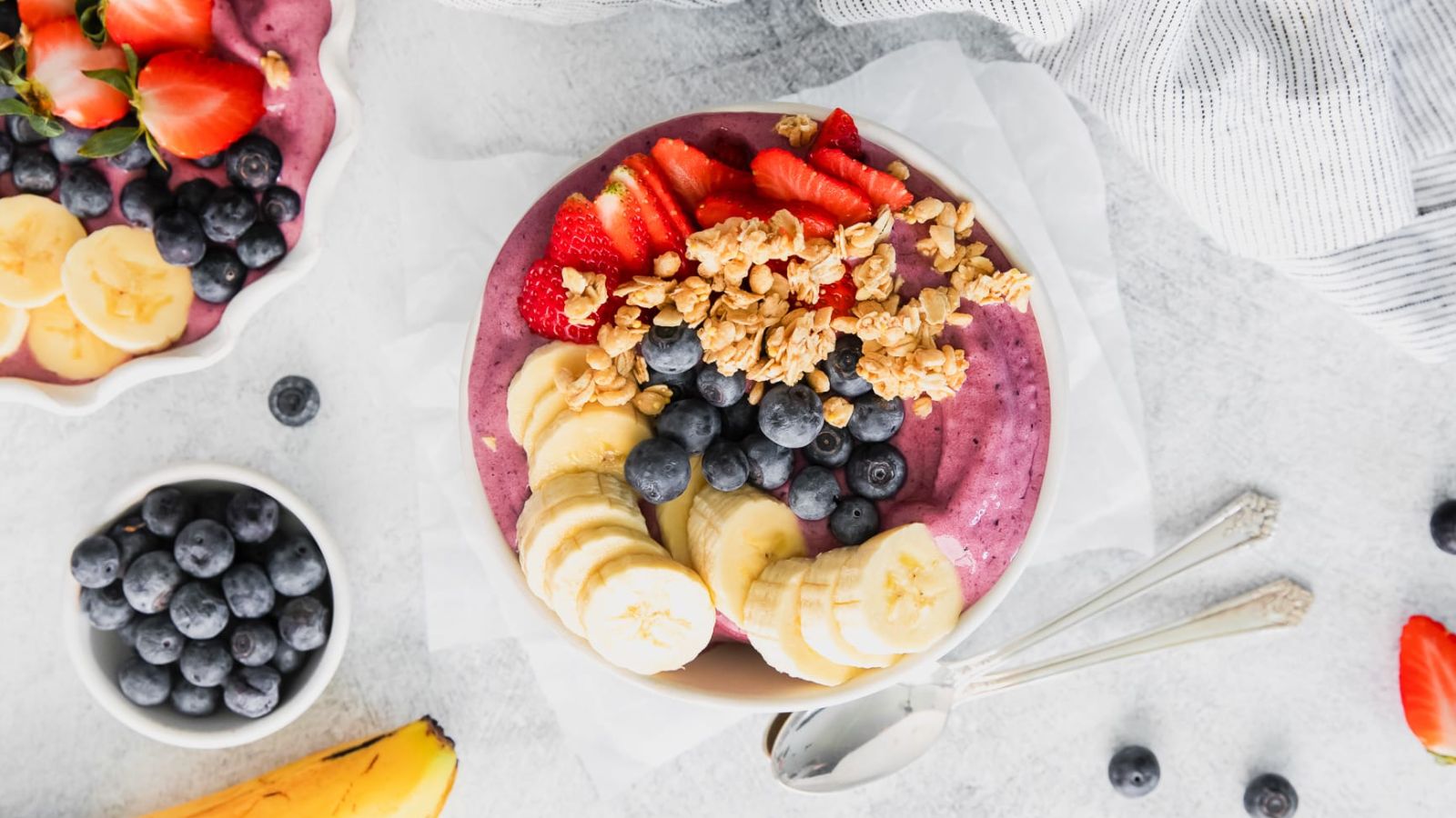 A purple smoothie bowl topped with banana slices, blueberries, sliced strawberries, and oats.