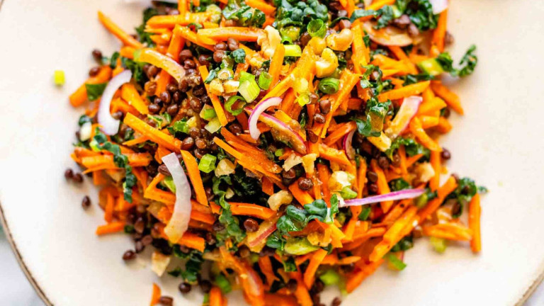 Shredded carrot salad on a plate with black lentils, green onion, and red onion.