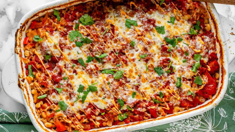 A casserole dish containing a rice casserole recipe covered in cheese and parsley.