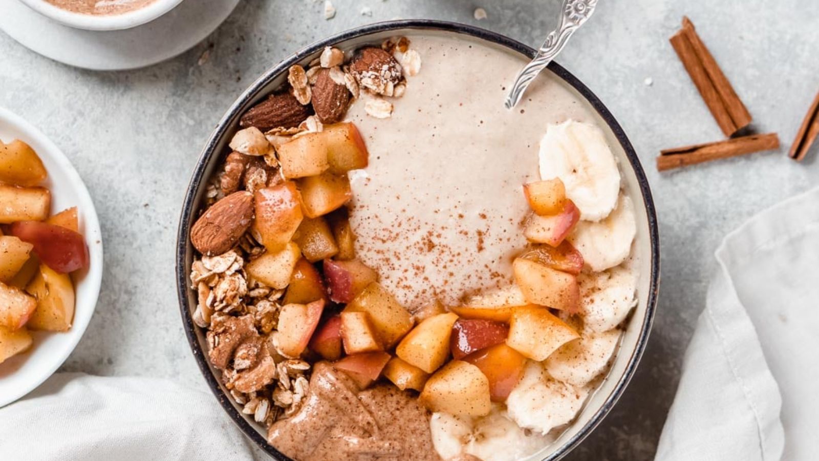 A beige smoothie bowl topped with granola, apples, nut butter, and banana slices.