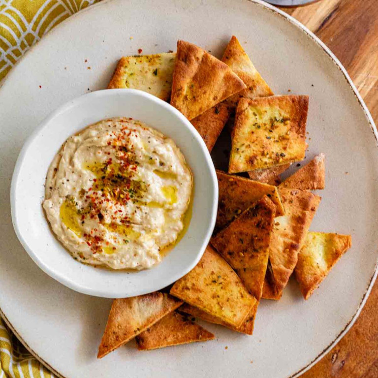 A plate with a bowl of hummus and pita chips beside it.