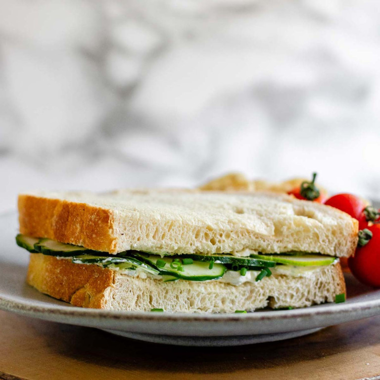 A sandwich with cucumbers beside tomatoes on a plate.