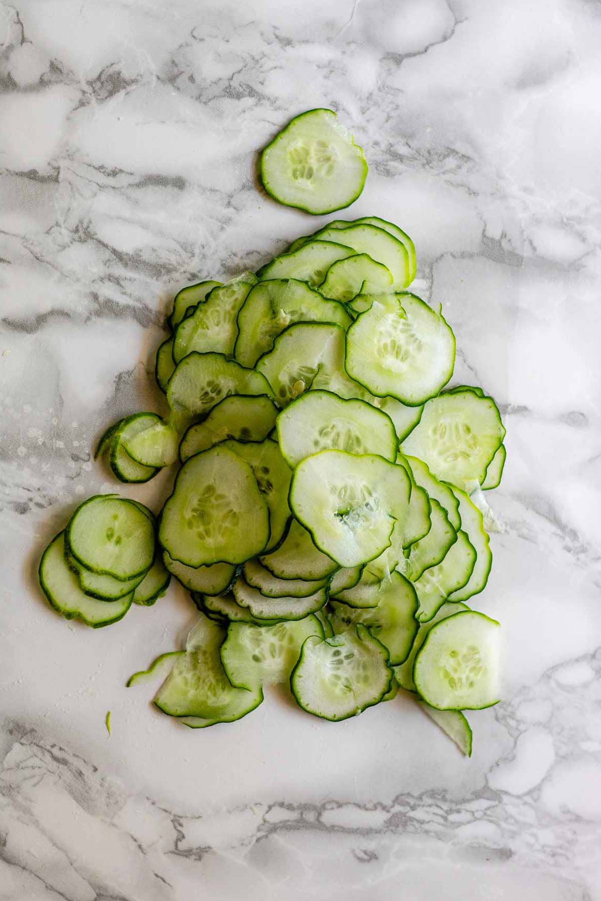 Sliced cucumber on a white marble counter.