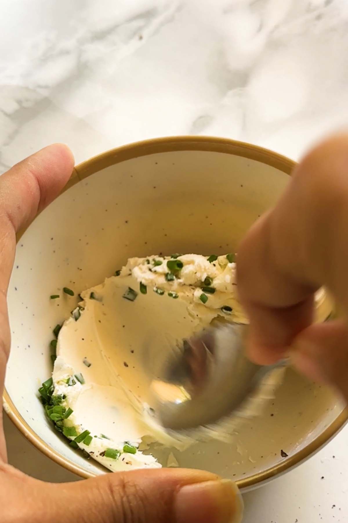 Cream cheese is mixed with a spoon in a bowl.