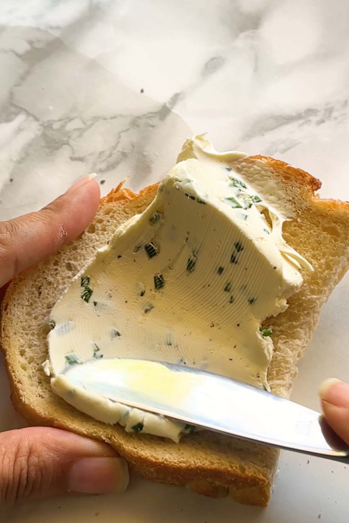 Cream cheese is spread with a knife on a slice of bread.