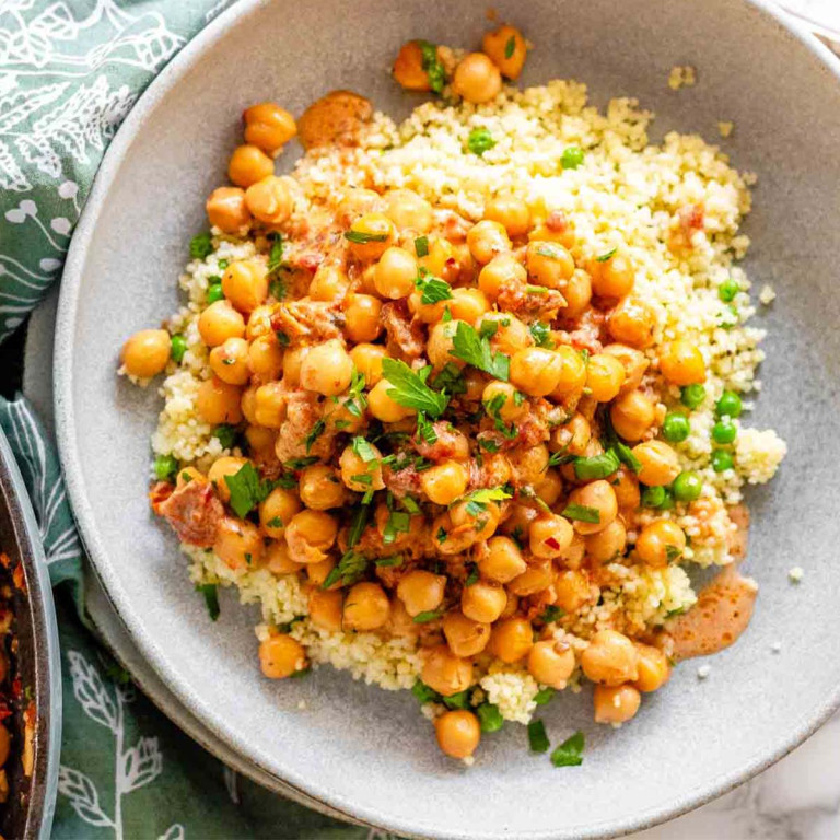 Chickpeas in a bowl on top of couscous and green peas.