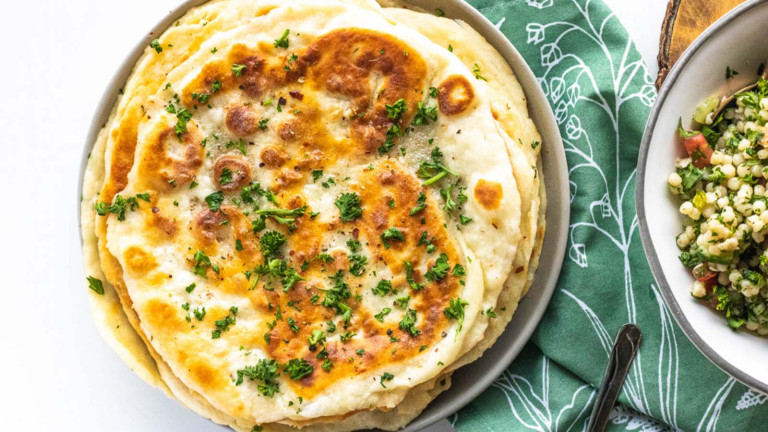Flatbreads stacked on a plate, topped with parsley beside a bowl of Israeli couscous.