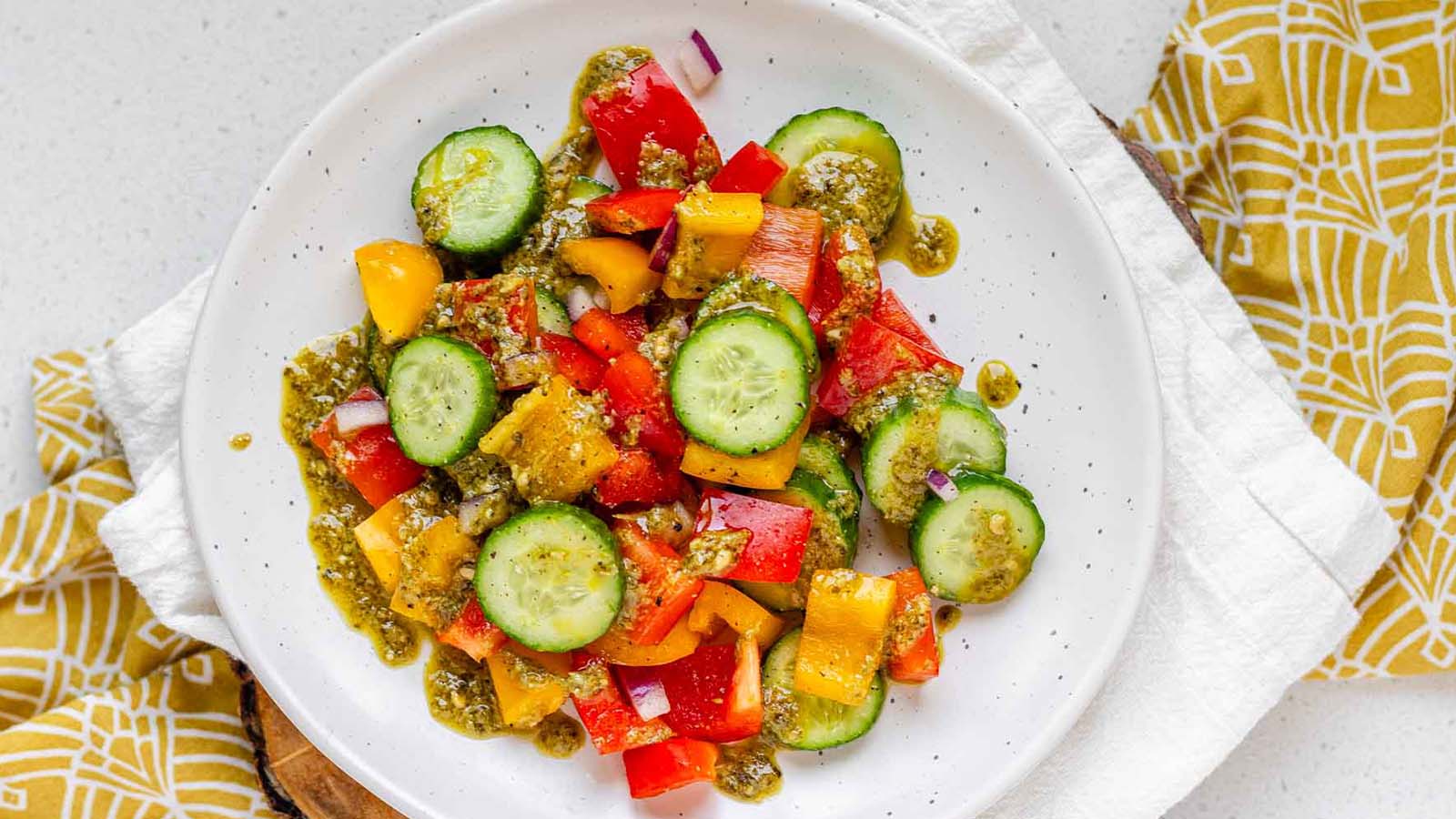 Sliced cucumbers and bell peppers on a plate with pesto dressing on top.