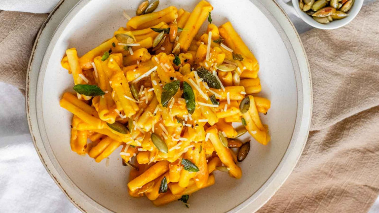 Short noodles in orange sauce topped with sage leaves, shredded cheese, and pumpkin seeds.
