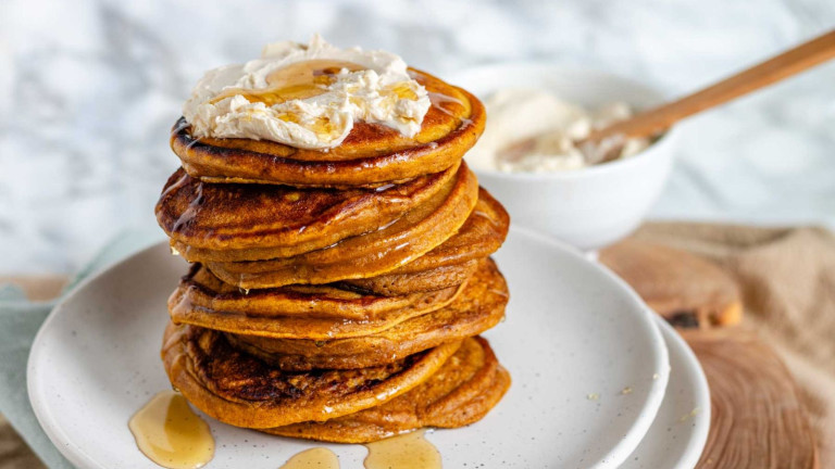 A stack of pancakes on a plate topped with whipped butter and syrup.