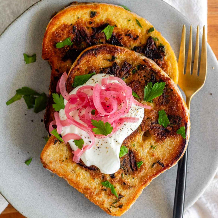 Toast topped with yogurt, pickled red onions, and parsley, on a plate with a fork.