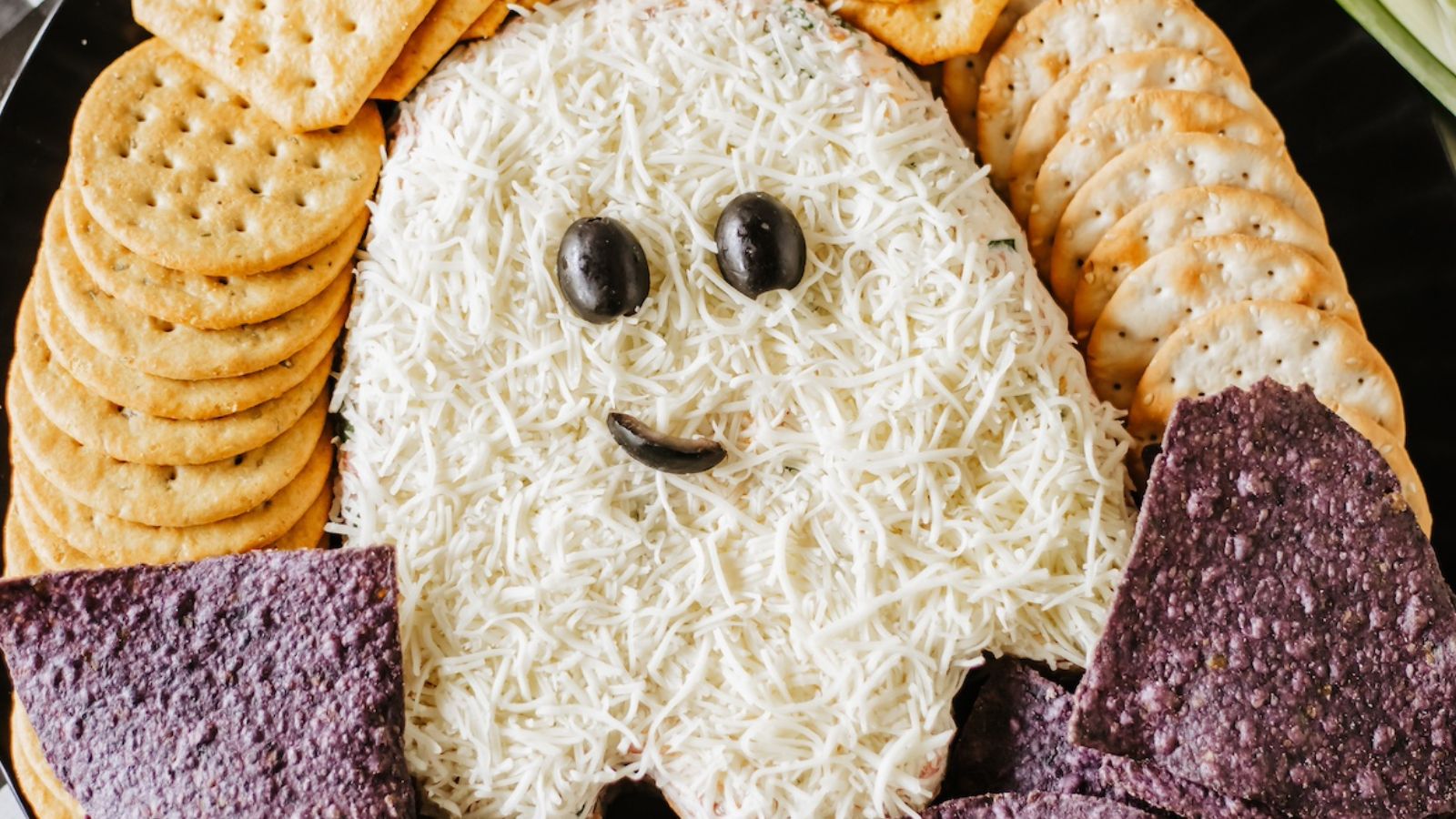 A flat cheese ball shaped like a ghost with olive eyes and an olive piece for a mouth.
