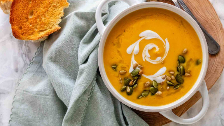Orange soup in a bowl with a white cream swirl and seeds on top.