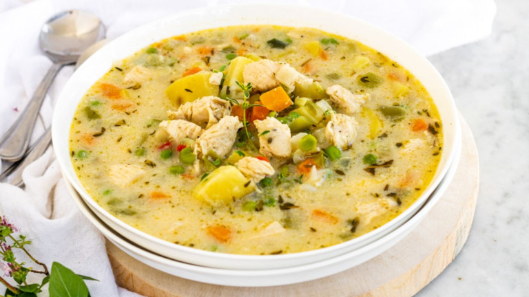 Creamy soup in a bowl with chicken, potatoes, vegetables, and herbs.