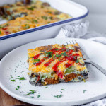 A square of a baked egg casserole on a plate, topped with a drizzle of sriracha.