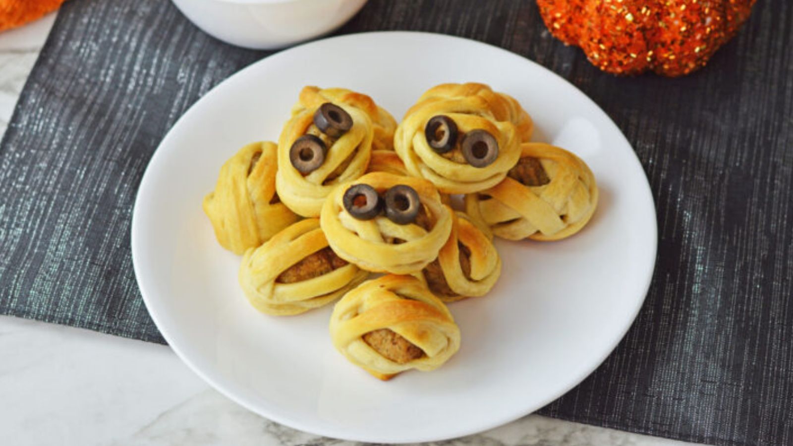 Meatballs wrapped in pastries with olive slices for eyes for Halloween.