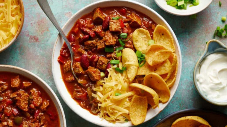 A bowl of chili with corn chips and cheese on top.