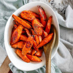 Sliced roasted glazed carrots topped with herbs, in a bowl with a wooden spoon.