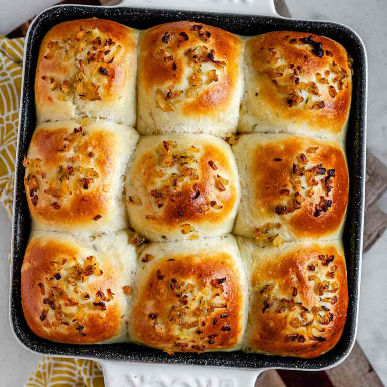 Dinner rolls in a pan topped with caramelized onions.