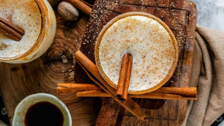 A creamy cocktail in glasses garnished with cinnamon sticks.