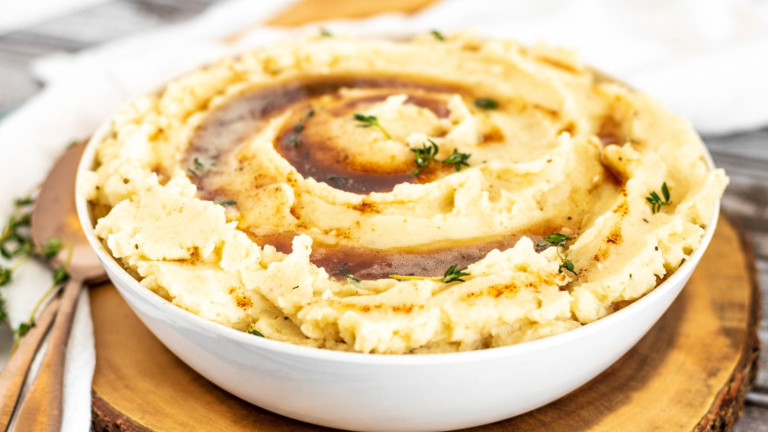 A bowl of mashed potatoes with a swirl of brown sauce on top.