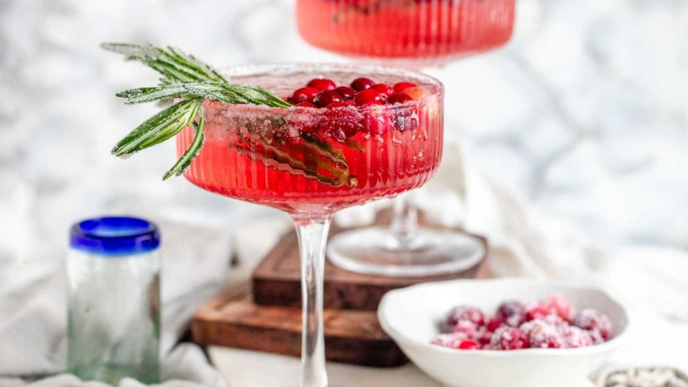 A red cocktail in glasses garnished with cranberries and rosemary.