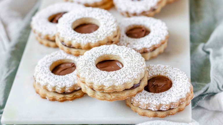 Sandwich cookies with a window showing a chocolate inside, topped with powdered sugar.